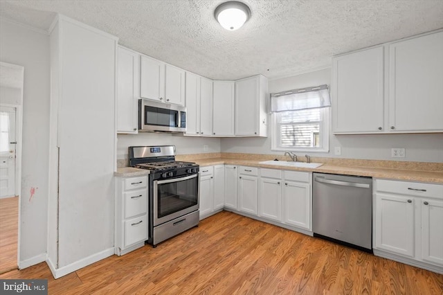 kitchen featuring appliances with stainless steel finishes, a sink, a textured ceiling, light countertops, and white cabinetry