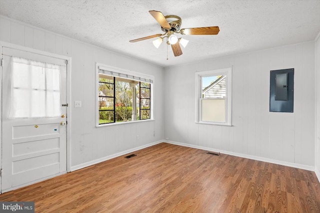 unfurnished room with electric panel, a textured ceiling, wood finished floors, plenty of natural light, and ceiling fan