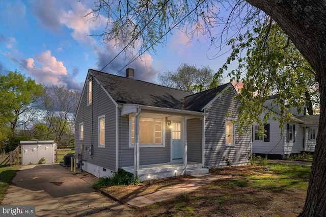 view of front of property with covered porch, an outbuilding, a chimney, a storage shed, and concrete driveway