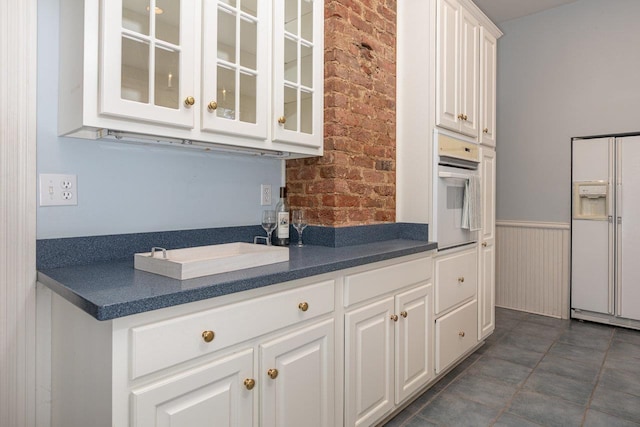 557 Wayne Ave S, Waynesboro, VA 22980 - kitchen with white appliances, brick wall, dark countertops, glass insert cabinets, and white cabinetry