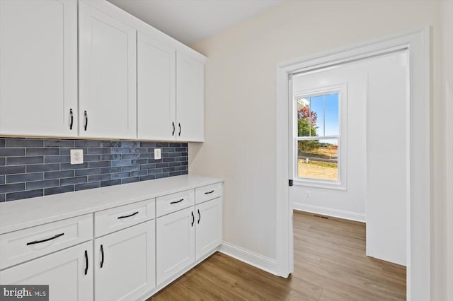 kitchen featuring baseboards, light wood-style floors, decorative backsplash, light countertops, and white cabinetry