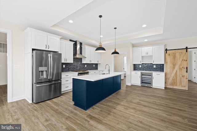 kitchen featuring appliances with stainless steel finishes, wall chimney exhaust hood, wine cooler, a tray ceiling, and recessed lighting