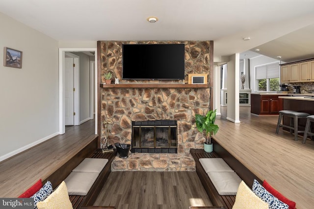 living room with wood finished floors, a stone fireplace, and baseboards