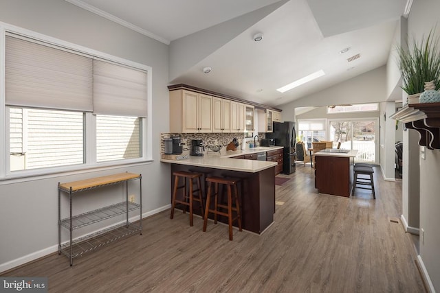 kitchen featuring a kitchen breakfast bar, a sink, wood finished floors, decorative backsplash, and light countertops