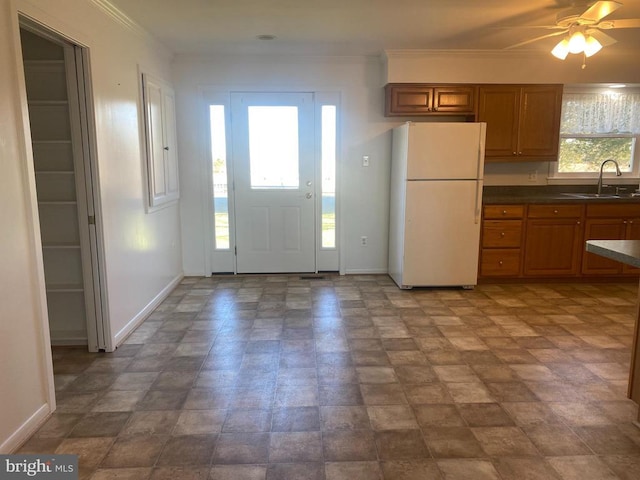  - kitchen featuring freestanding refrigerator, a sink, brown cabinets, dark countertops, and ornamental molding