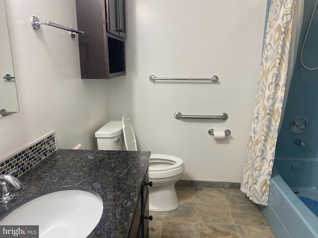  - bathroom featuring toilet, vanity, stone finish flooring, shower / tub combo, and baseboards