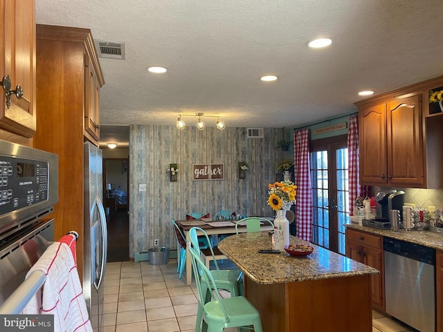  - kitchen with stainless steel appliances, a center island, a baseboard radiator, brown cabinetry, and a textured ceiling