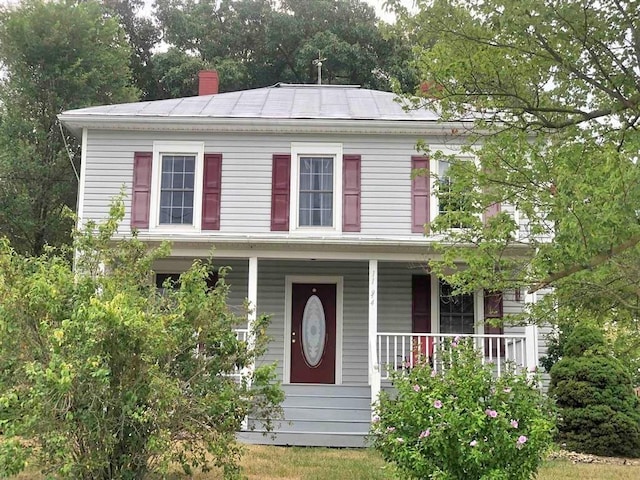 colonial house featuring a chimney and covered porch