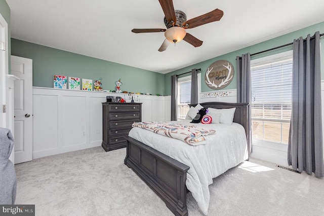 carpeted bedroom featuring a wainscoted wall, ceiling fan, and a decorative wall