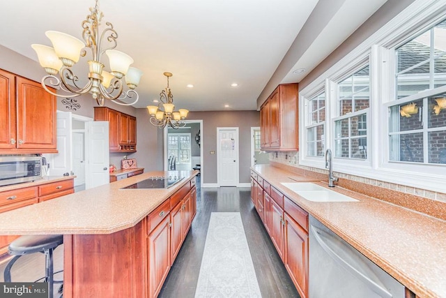 kitchen with appliances with stainless steel finishes, a sink, a kitchen island with sink, light countertops, and a notable chandelier