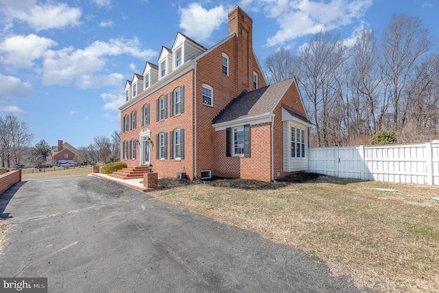 view of home's exterior featuring brick siding, a lawn, a chimney, and fence