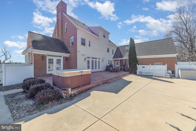 back of house featuring french doors, brick siding, fence, and a hot tub