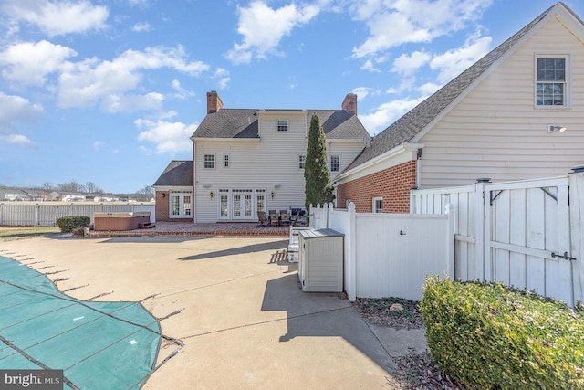 rear view of house with french doors, a patio area, brick siding, and a hot tub