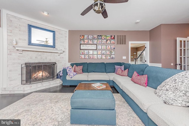 living area with a ceiling fan, a brick fireplace, visible vents, and stairs