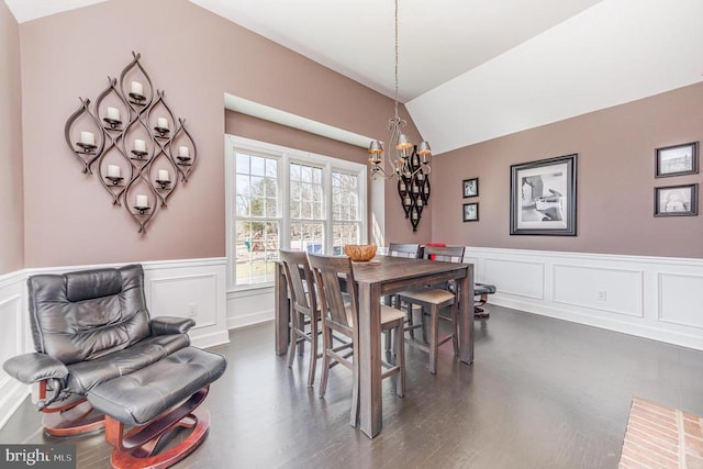 dining space with lofted ceiling, dark wood-type flooring, wainscoting, and a notable chandelier