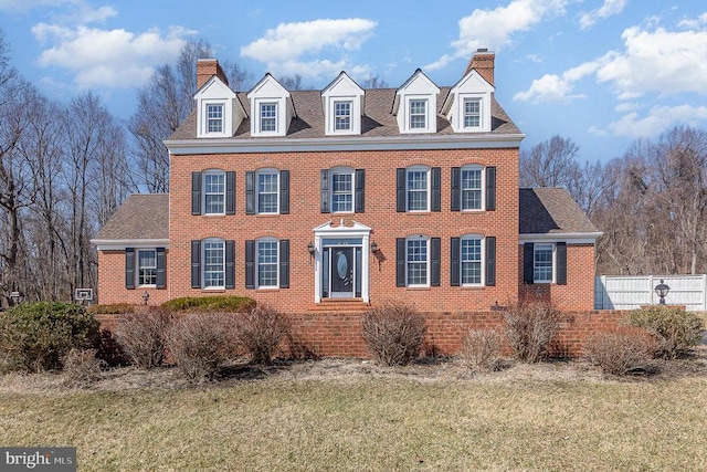 view of front of house with brick siding, roof with shingles, a chimney, fence, and a front lawn