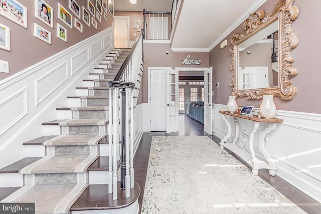 entryway featuring stairway, a decorative wall, crown molding, and wainscoting