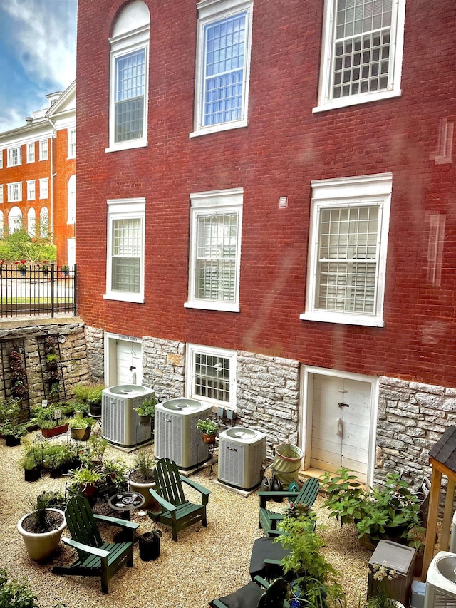 rear view of property featuring central AC unit, stone siding, and fence