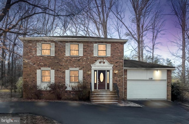 colonial house with aphalt driveway, an attached garage, and brick siding