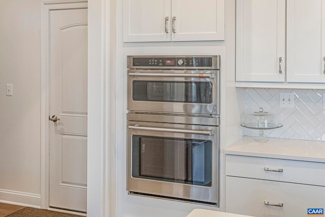 kitchen featuring double oven, decorative backsplash, white cabinets, light countertops, and baseboards