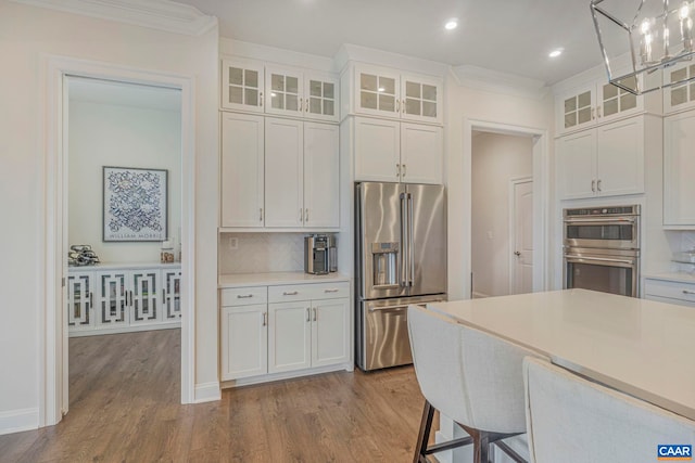 kitchen featuring appliances with stainless steel finishes, white cabinetry, wood finished floors, tasteful backsplash, and light countertops