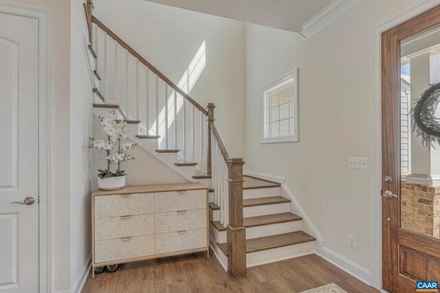 staircase featuring wood finished floors, crown molding, and baseboards