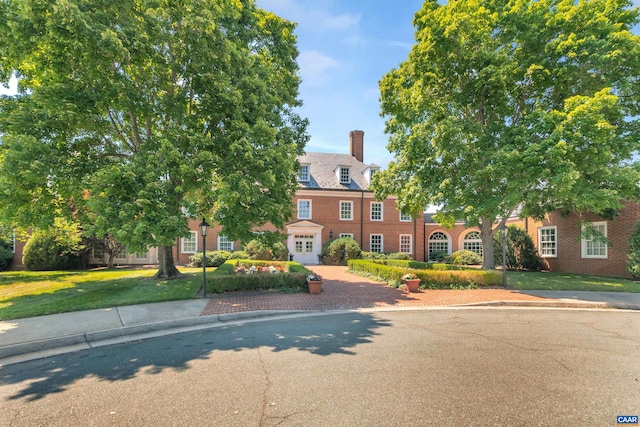 view of front of home featuring a chimney, brick siding, and a front yard