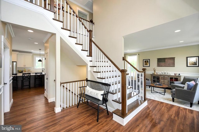  - stairs with wood finished floors, recessed lighting, ornamental molding, and a high ceiling