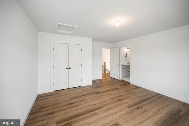  - unfurnished bedroom featuring wood finished floors, baseboards, a closet, and attic access