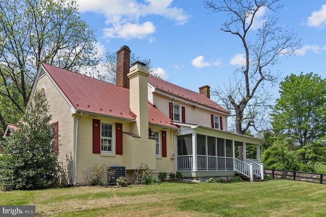  - back of property featuring a chimney, a sunroom, stucco siding, central AC, and metal roof