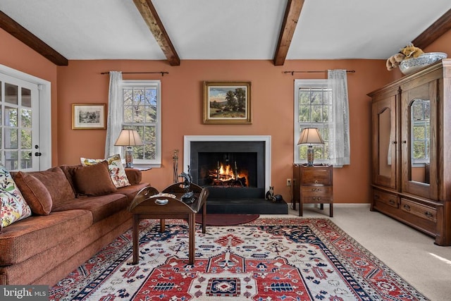  - living room featuring beam ceiling, a warm lit fireplace, carpet floors, and baseboards