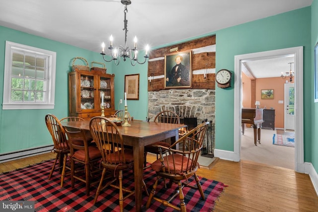  - dining room featuring a chandelier, hardwood / wood-style flooring, a stone fireplace, and baseboards