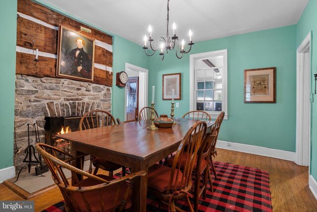  - dining space featuring baseboards, a chandelier, wood finished floors, and a fireplace