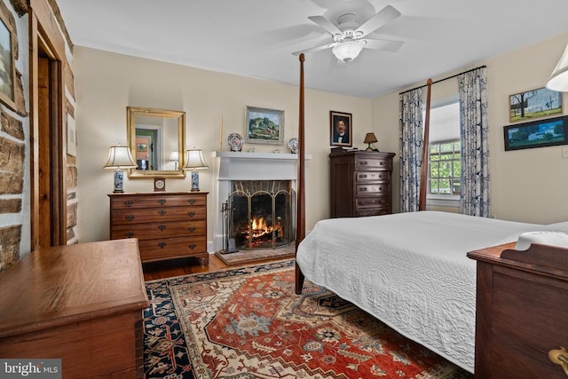  - bedroom with a lit fireplace, wood finished floors, and a ceiling fan