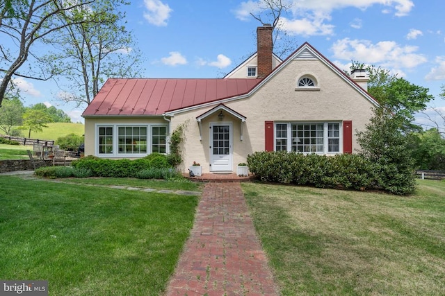  - view of front facade with a standing seam roof, stucco siding, a chimney, and a front yard