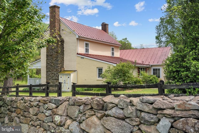  - view of home's exterior with a standing seam roof, stucco siding, metal roof, a chimney, and fence