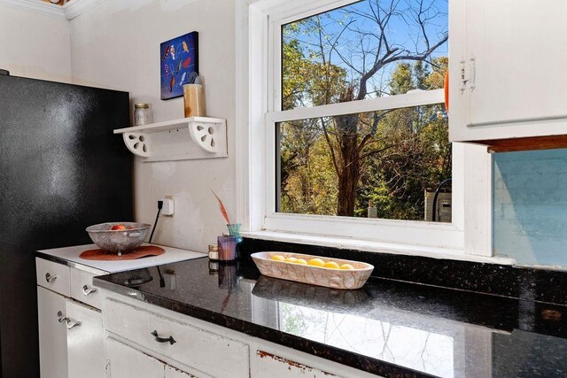 kitchen featuring white cabinetry, dark stone counters, and black fridge