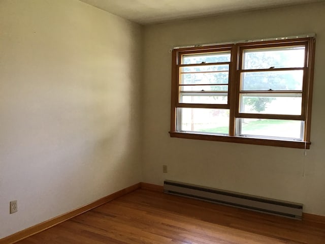spare room with a baseboard heating unit, baseboards, and wood finished floors