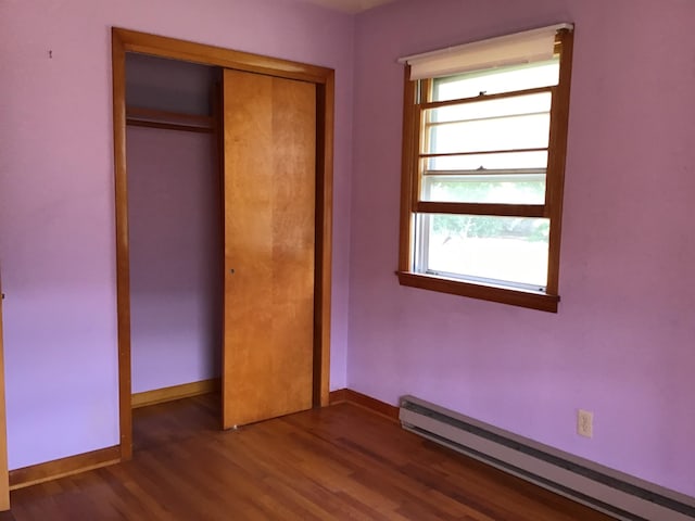 unfurnished bedroom featuring multiple windows, wood finished floors, baseboards, and a baseboard heating unit