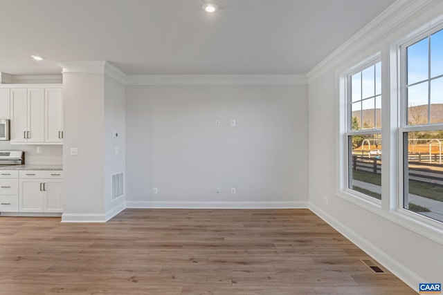 empty room with crown molding, light wood-type flooring, and baseboards