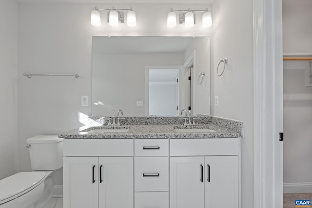 full bathroom featuring double vanity, toilet, baseboards, and a sink