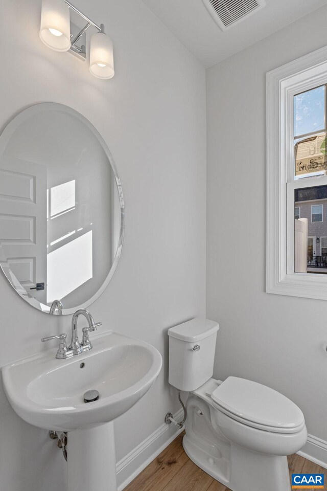 bathroom with toilet, wood finished floors, a sink, visible vents, and baseboards