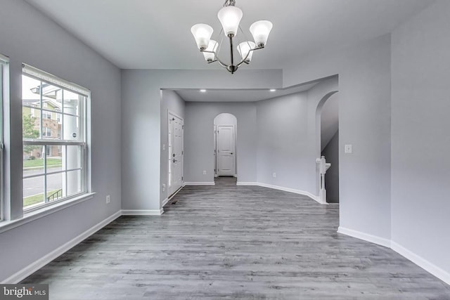  - unfurnished room featuring arched walkways, wood finished floors, and a chandelier