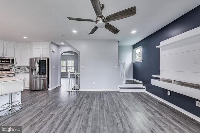  - unfurnished living room featuring arched walkways, a ceiling fan, wood finished floors, recessed lighting, and stairs