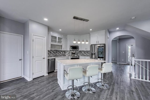  - kitchen featuring stainless steel appliances, arched walkways, a kitchen island, white cabinetry, and dark wood-style flooring