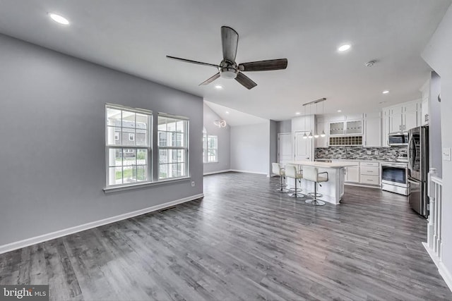  - kitchen with appliances with stainless steel finishes, open floor plan, a breakfast bar, white cabinetry, and tasteful backsplash