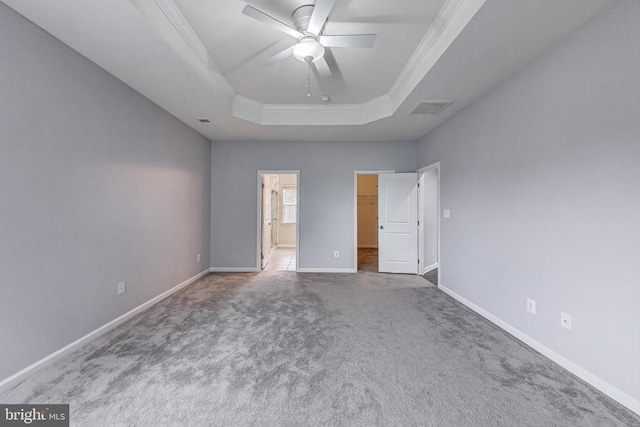  - unfurnished bedroom featuring crown molding, a tray ceiling, carpet flooring, a spacious closet, and a ceiling fan