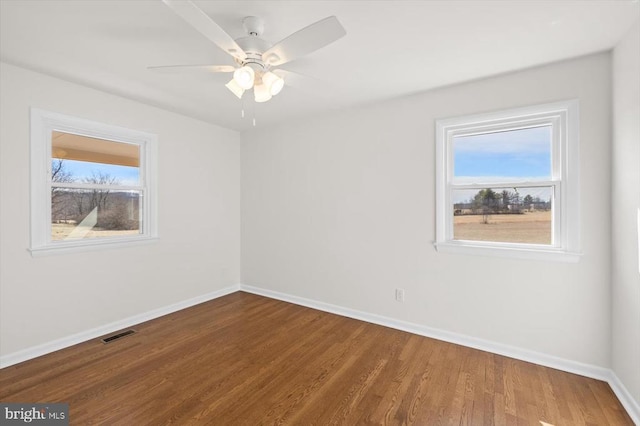 empty room with visible vents, a ceiling fan, baseboards, and wood finished floors