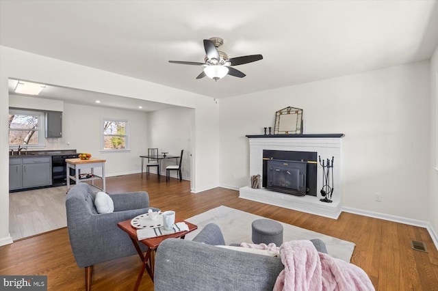 living area with visible vents, baseboards, a brick fireplace, and wood finished floors