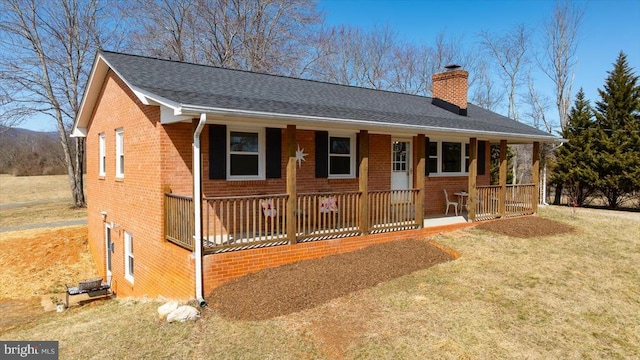 view of front of property featuring a front yard, covered porch, a shingled roof, a chimney, and brick siding